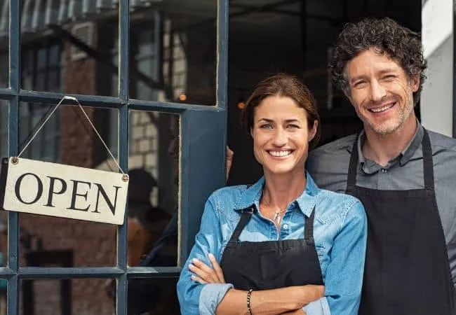 Male and female business owners standing in front of a door with an open sign.